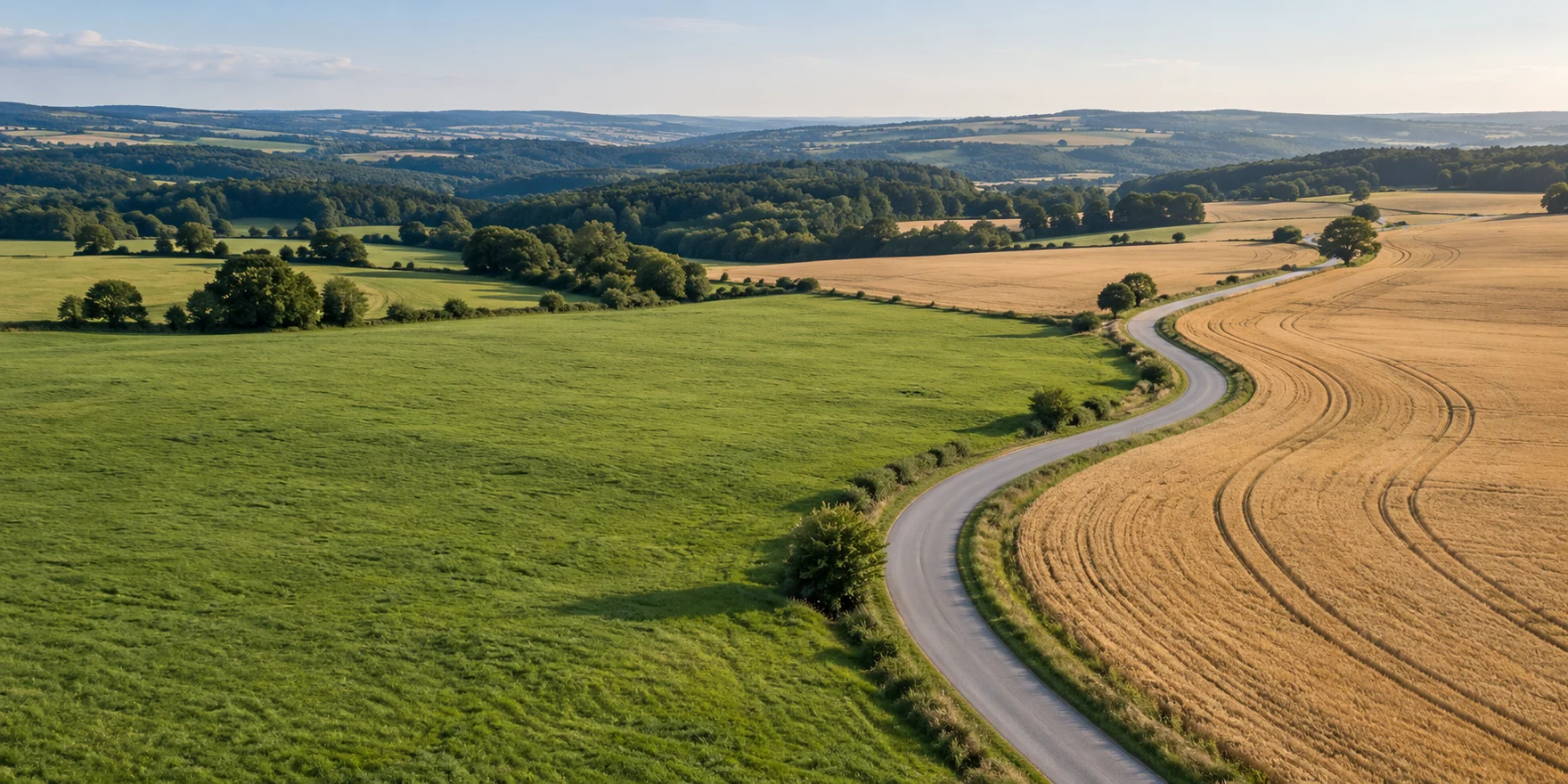 Eine Landstraße verbindet grüne und goldene Felder in einer europäischen Hügellandschaft